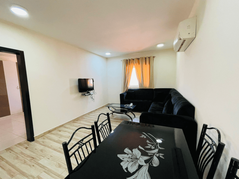 Apartment for rent: Modern living room with black sofa and dining table, wooden flooring, wall-mounted tv, and air conditioner.