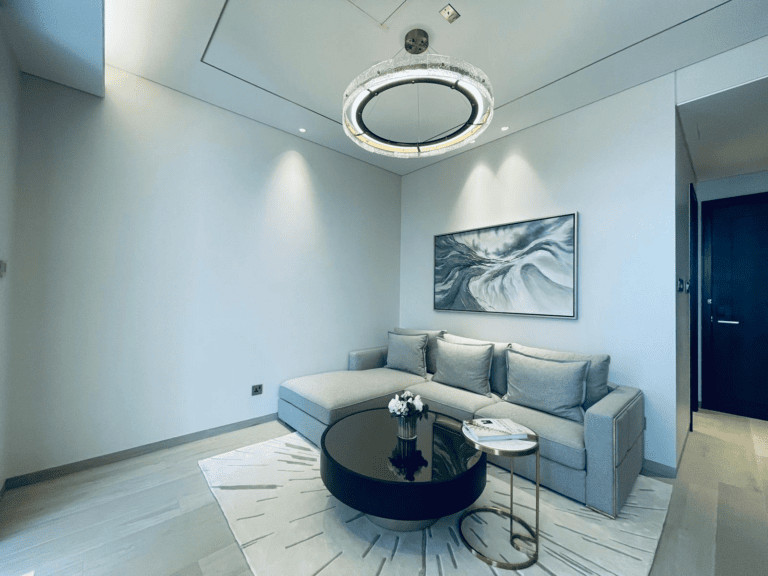 Modern apartment living room with a curved gray sofa, round black coffee table, and a large abstract painting on the wall, under an elegant circular chandelier.