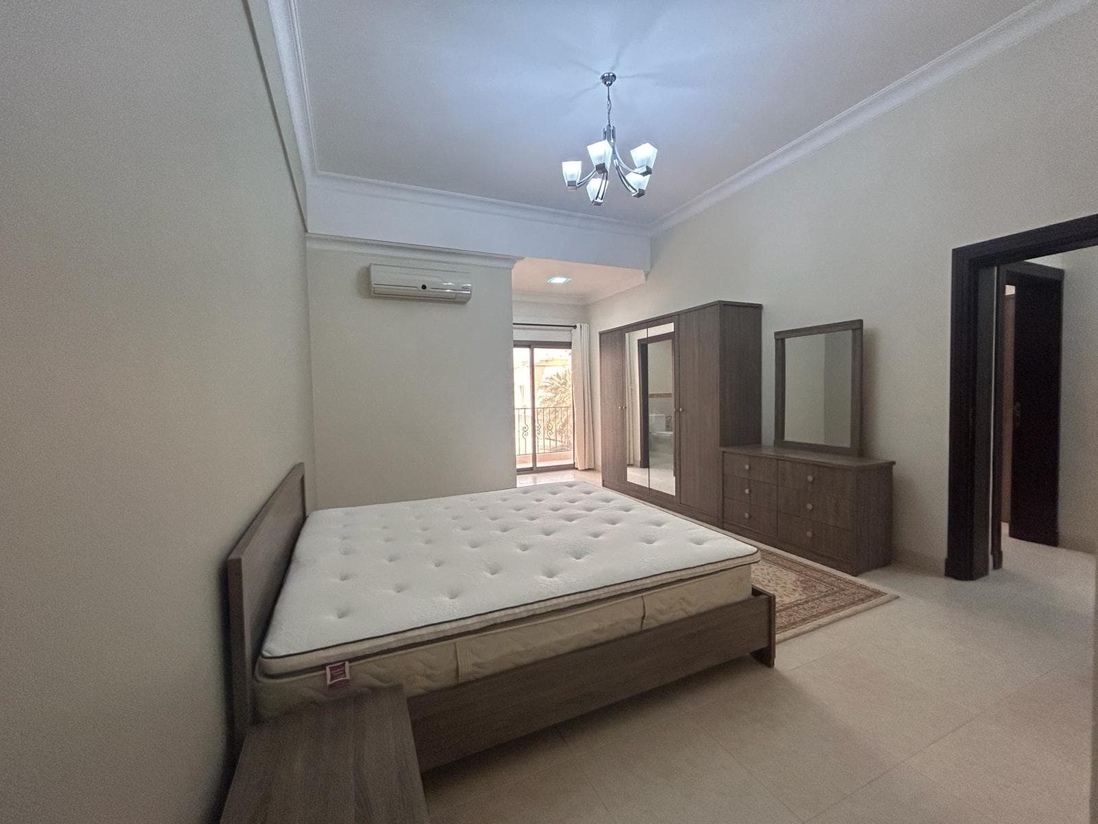 A luxury fully-furnished 2 BDR apartment bedroom with a large bed, dresser, air conditioning unit, and access to a balcony.