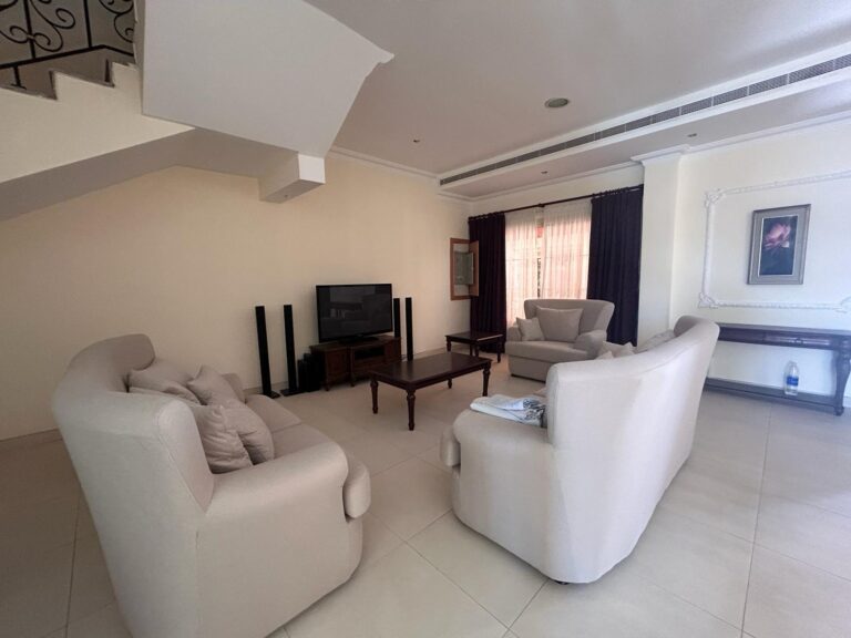 غرفة معيشة واسعة بها أرائك بيضاء وتلفزيون وديكور بسيط.