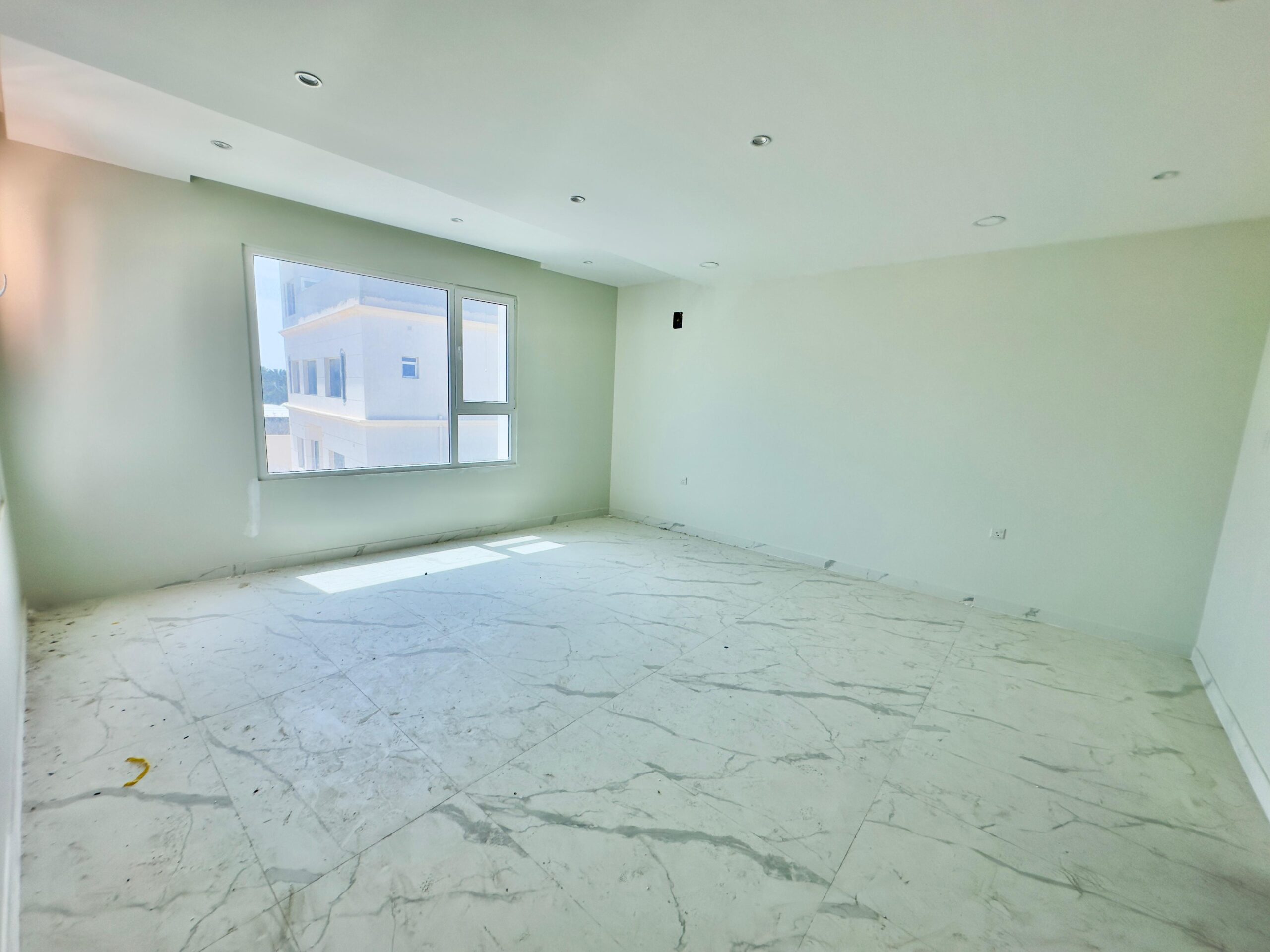 Empty room with white marble flooring and white walls, featuring a large window with a view of neighboring buildings.