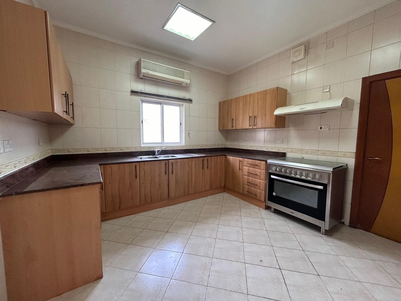 An empty kitchen with wooden cabinets, black countertops, a white stove, and a tile floor in a 3 BDR Villa, seen in natural daylight.