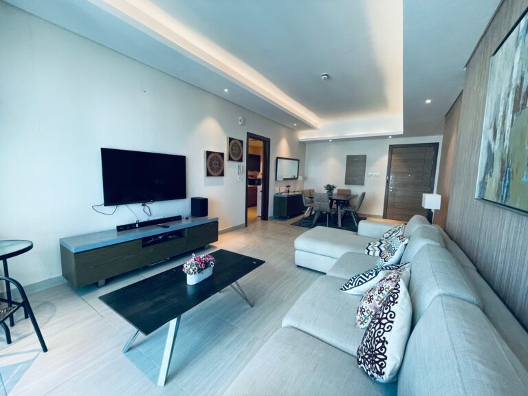 Modern living room with a large sofa, coffee table, and television, leading to a dining area and a kitchen in the Auto Draft background.