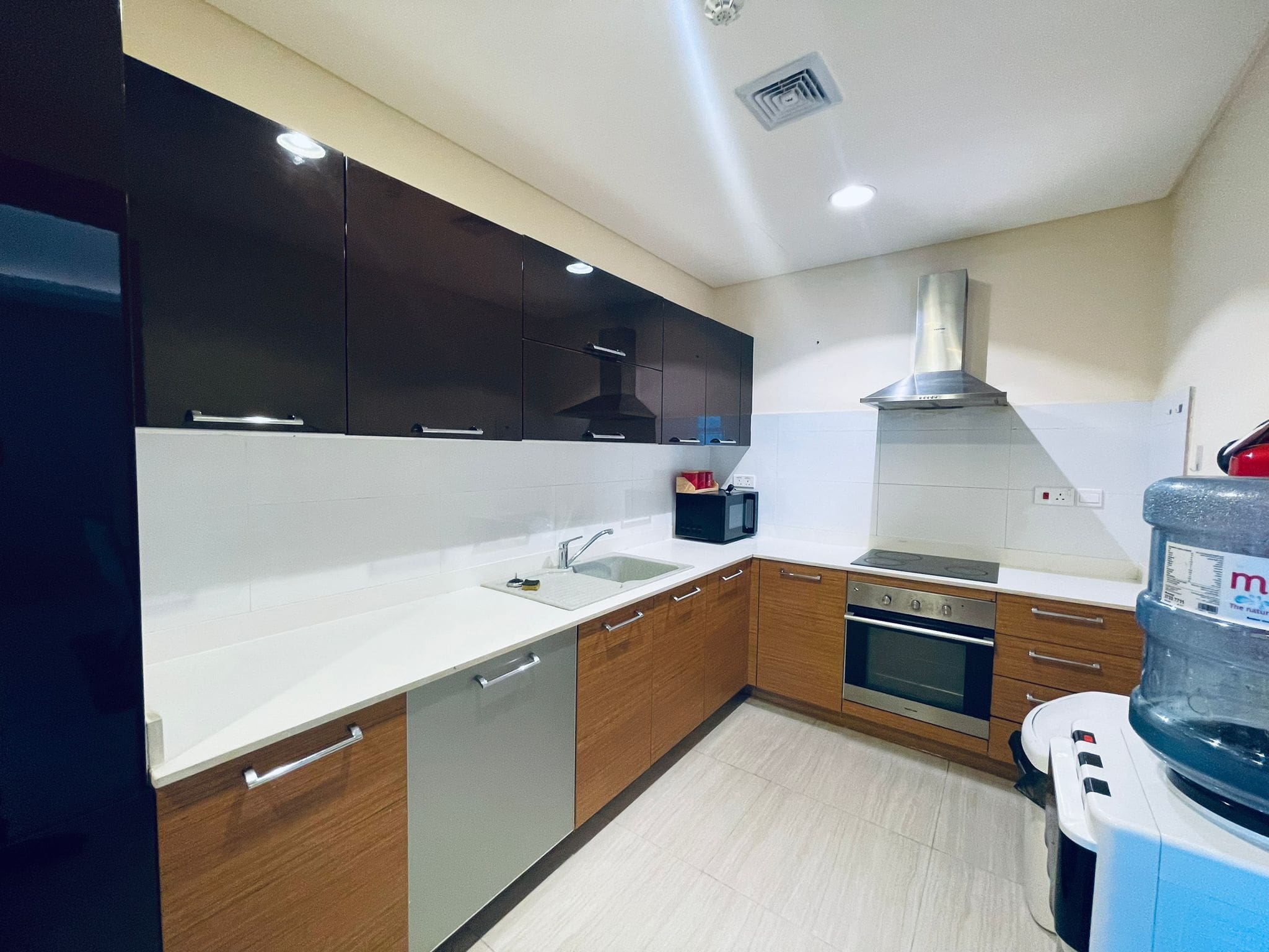 Modern kitchen interior with dark cabinets, white countertops, built-in appliances, and a stainless steel range hood. This auto draft system ensures efficient ventilation, keeping the space fresh and smoke-free.