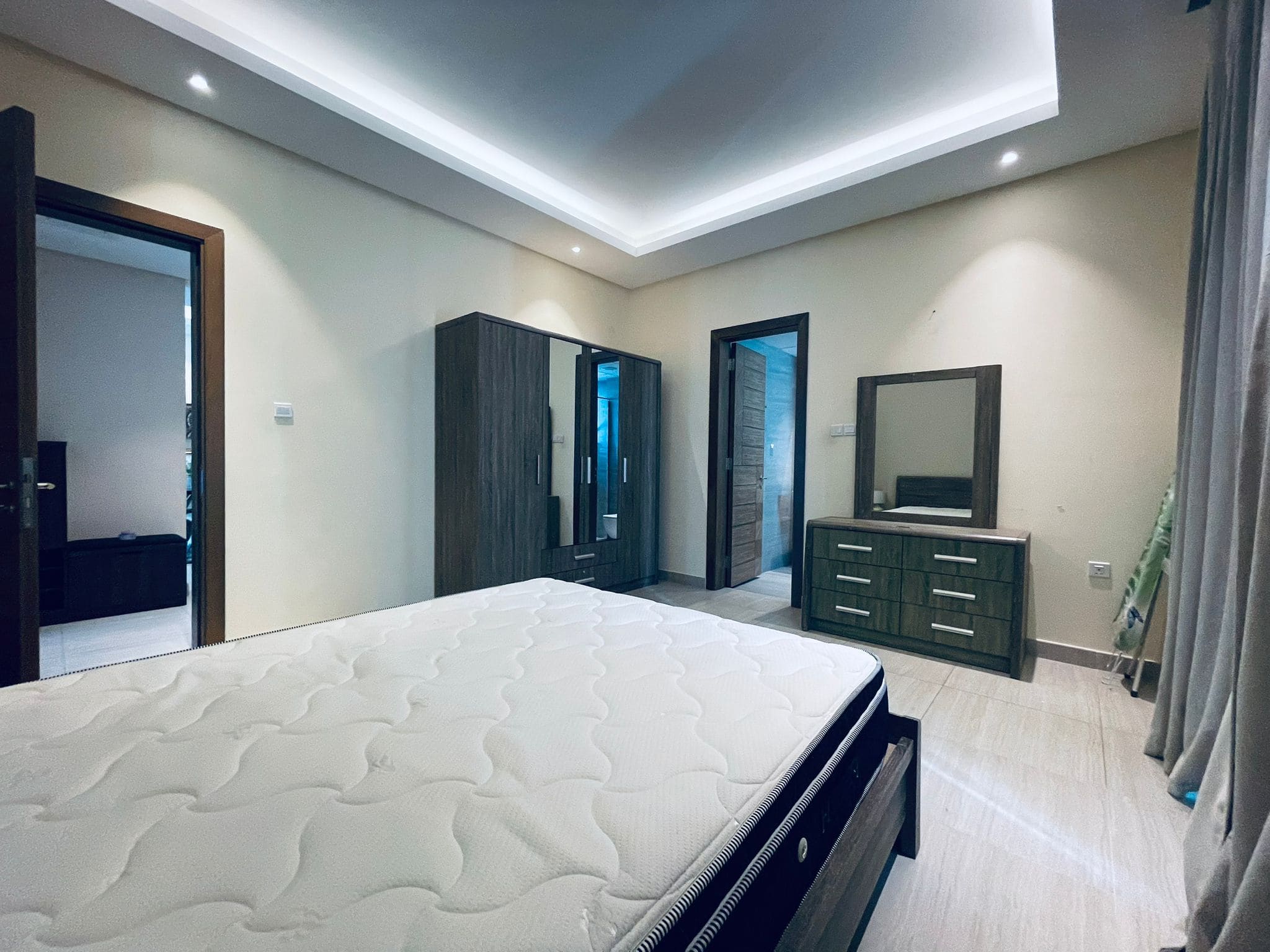 Modern bedroom with a large bed, dark wood furniture, and recessed ceiling lighting. Two doors and an auto draft mirror are also visible.