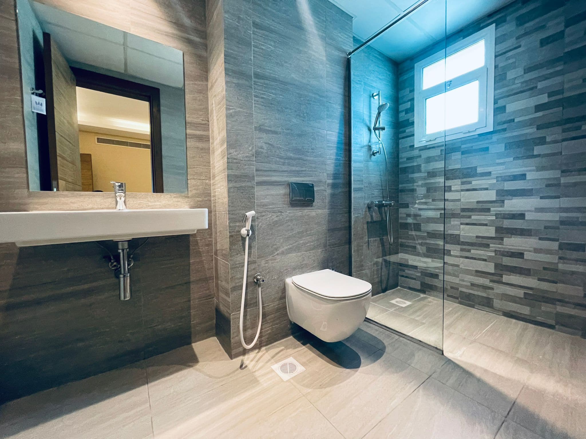 Modern bathroom interior featuring a wall-mounted toilet, glass shower door, and a large mirror over a sink, with grey and brown Auto Draft walls.