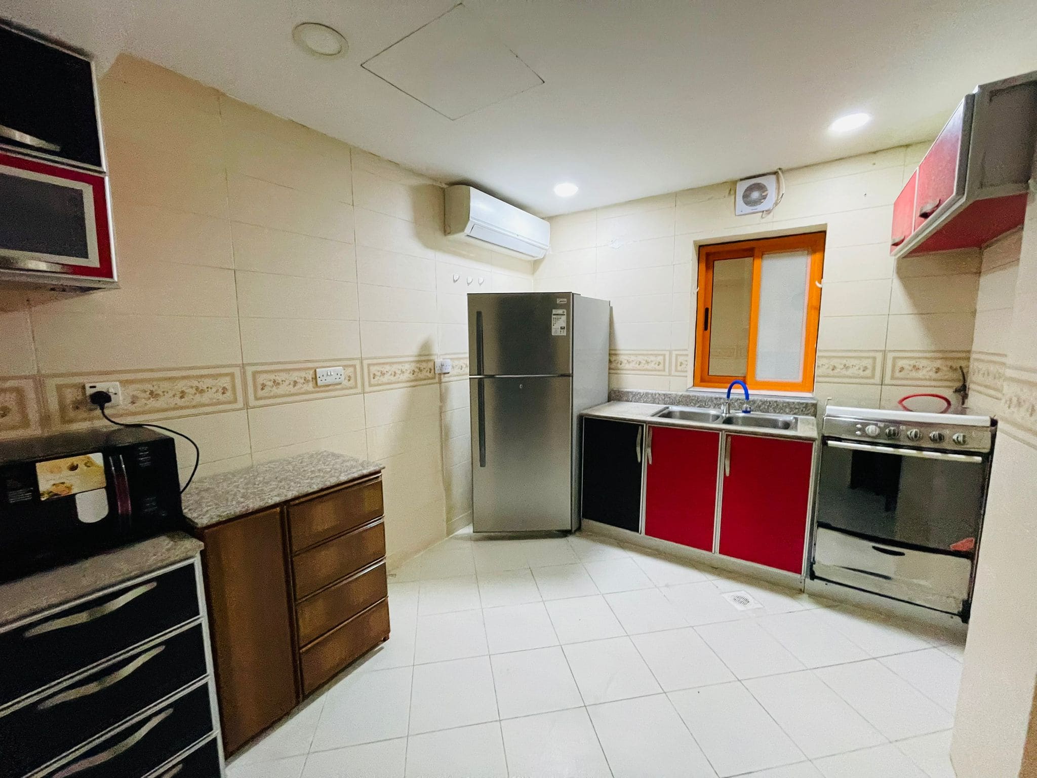 A modern kitchen in an available studio for rent, with red and black cabinets, stainless steel refrigerator, and a microwave on the counter.