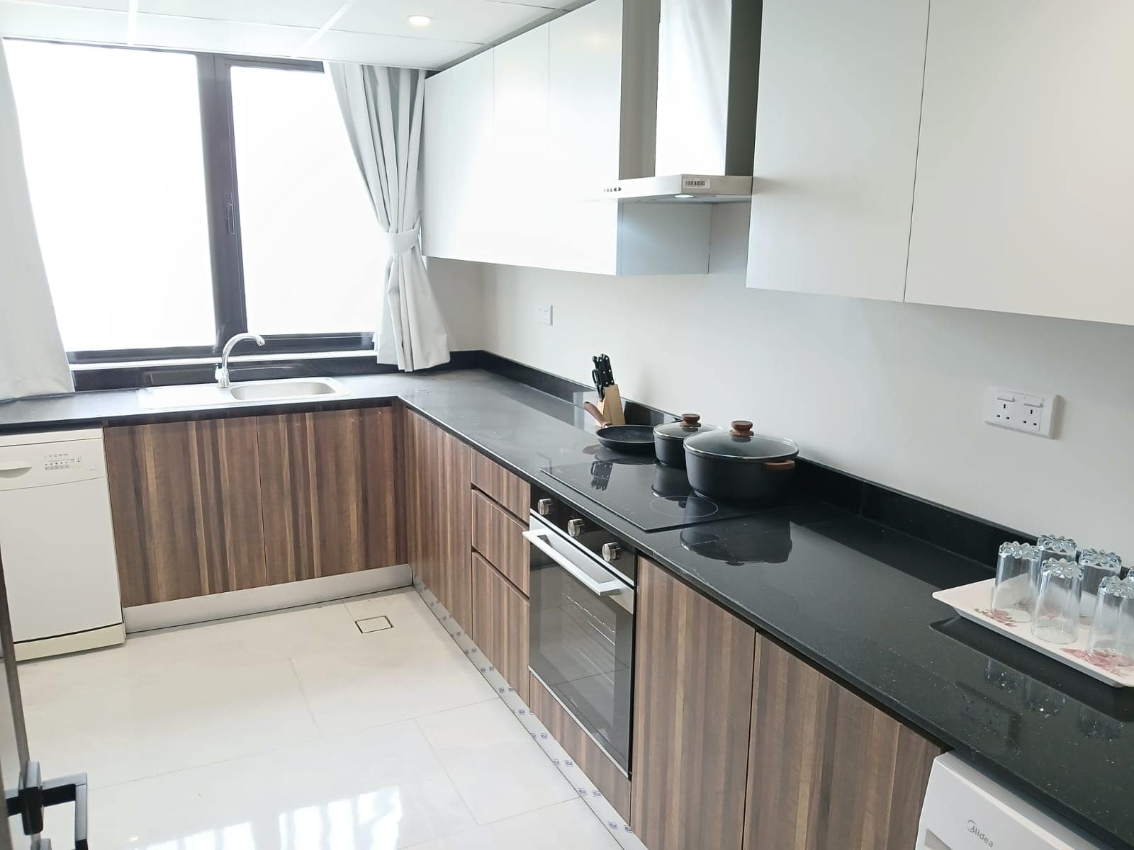 Modern kitchen with white and wooden cabinets, black countertop, sink, and appliances including a dishwasher.