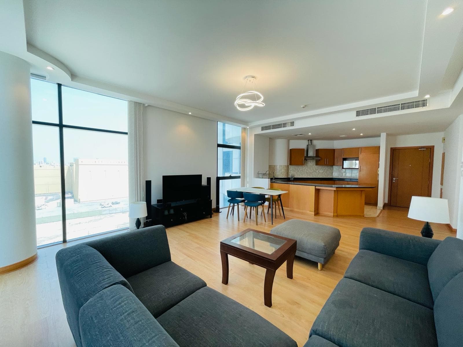 Luxury apartment living area with sofas, a coffee table, dining area, and kitchenette, large windows providing ample natural light in the Sanabis area.