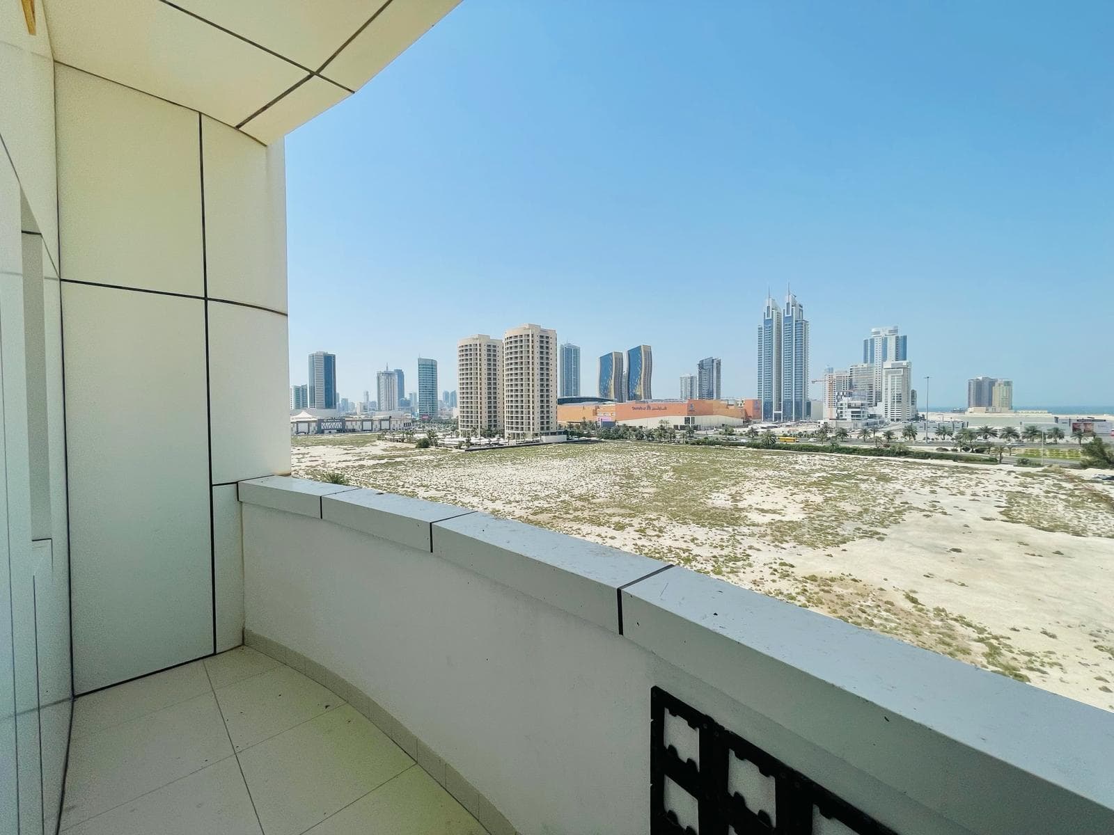 View from a luxury apartment balcony in the Sanabis area, showing a sandy landscape and city skyline with modern high-rise buildings under a clear blue sky.