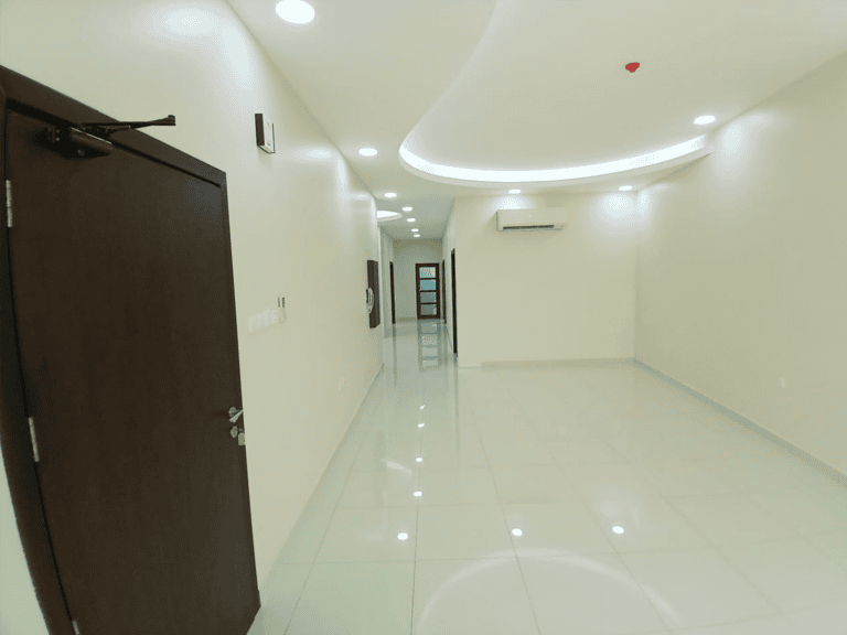 Modern hallway in a brand new apartment with glossy white floors, curved ceilings with recessed lighting, and multiple doors, one partially open.