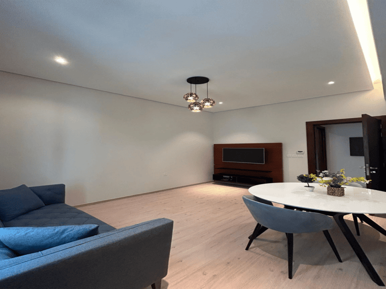 يتميز التصميم الداخلي لغرفة المعيشة الحديثة بأريكة زرقاء وطاولة مستديرة وأرضية خشبية وثريا كروية مزخرفة.