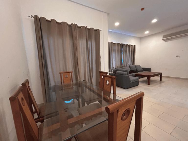 غرفة معيشة حديثة تحتوي على طاولة طعام زجاجية، وكراسي خشبية، وأريكة رمادية على الحائط محاطة بستائر بطول الأرضية.