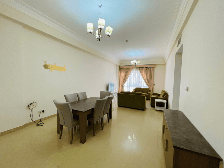 Modern, spacious furnished apartment in the Sanabis area with a dining table, chairs, and a cozy seating area with sofas under a chandelier and beside curtained windows.