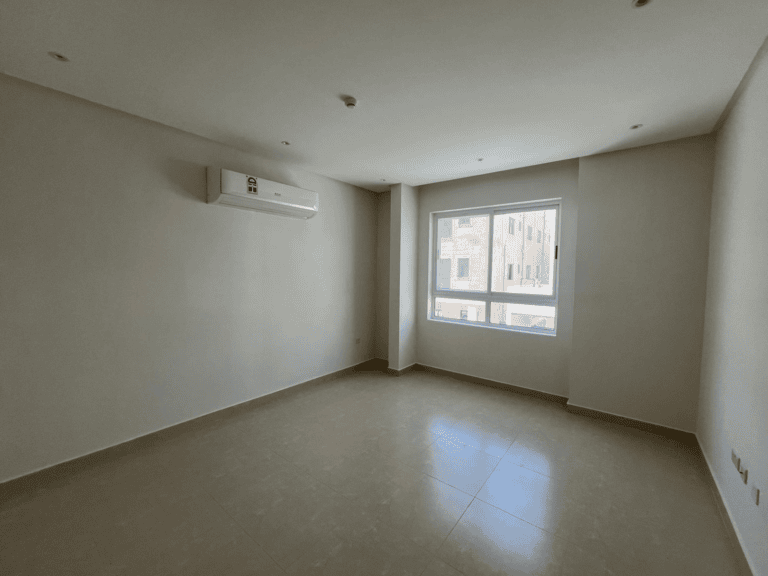 Empty modern flat for rent in AL Hidd with white walls, a large window, and an air conditioning unit mounted on the wall.