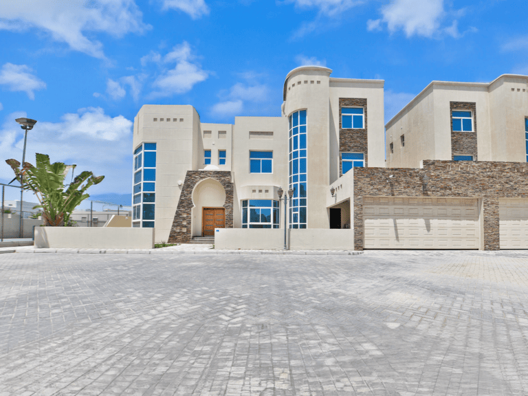 Luxury villa with a white exterior, stone accents, and large windows, situated in the Janbiya area under a clear blue sky.