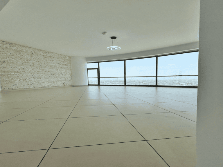 Empty 2 bedroom apartment for rent with large windows, white tiled floor, and exposed textured concrete wall, overlooking a cityscape.
