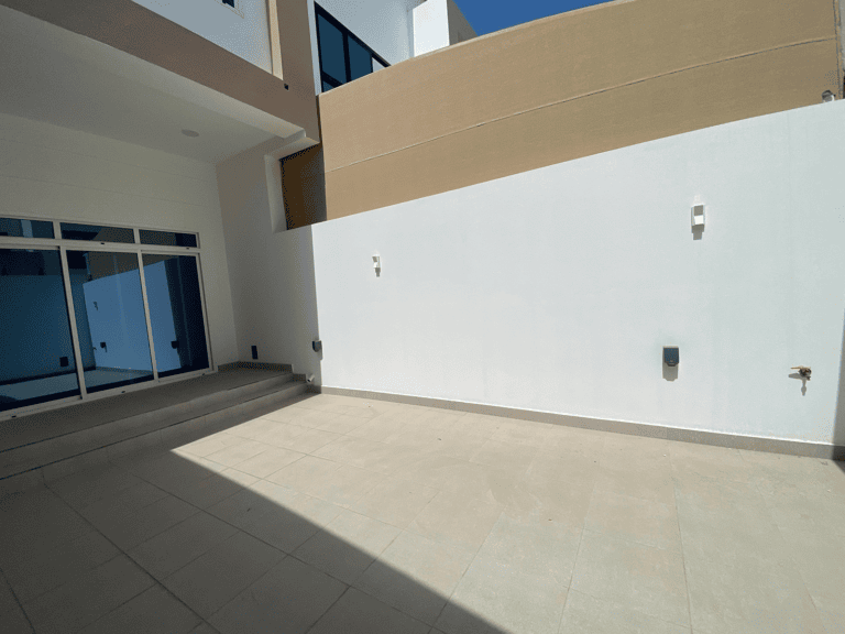 Courtyard of a modern villa for sale with beige tiles and white walls, featuring two doors and minimalistic light fixtures.