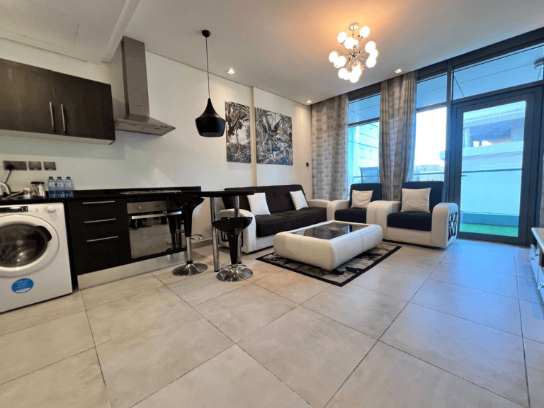 Luxury apartment interior featuring an open-plan kitchen with dark cabinets and a living area with a brown sectional sofa, white chairs, and tasteful decor.