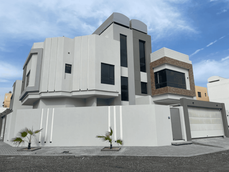 A modern two-story villa for sale featuring a combination of plaster and stone facades, large windows, and a closed garage, located in Bani Jamra under a clear sky.