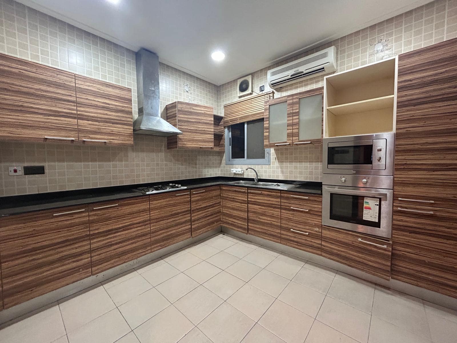 Modern 3 BDR apartment kitchen with wood cabinets, black countertops, built-in appliances, and a tiled floor.