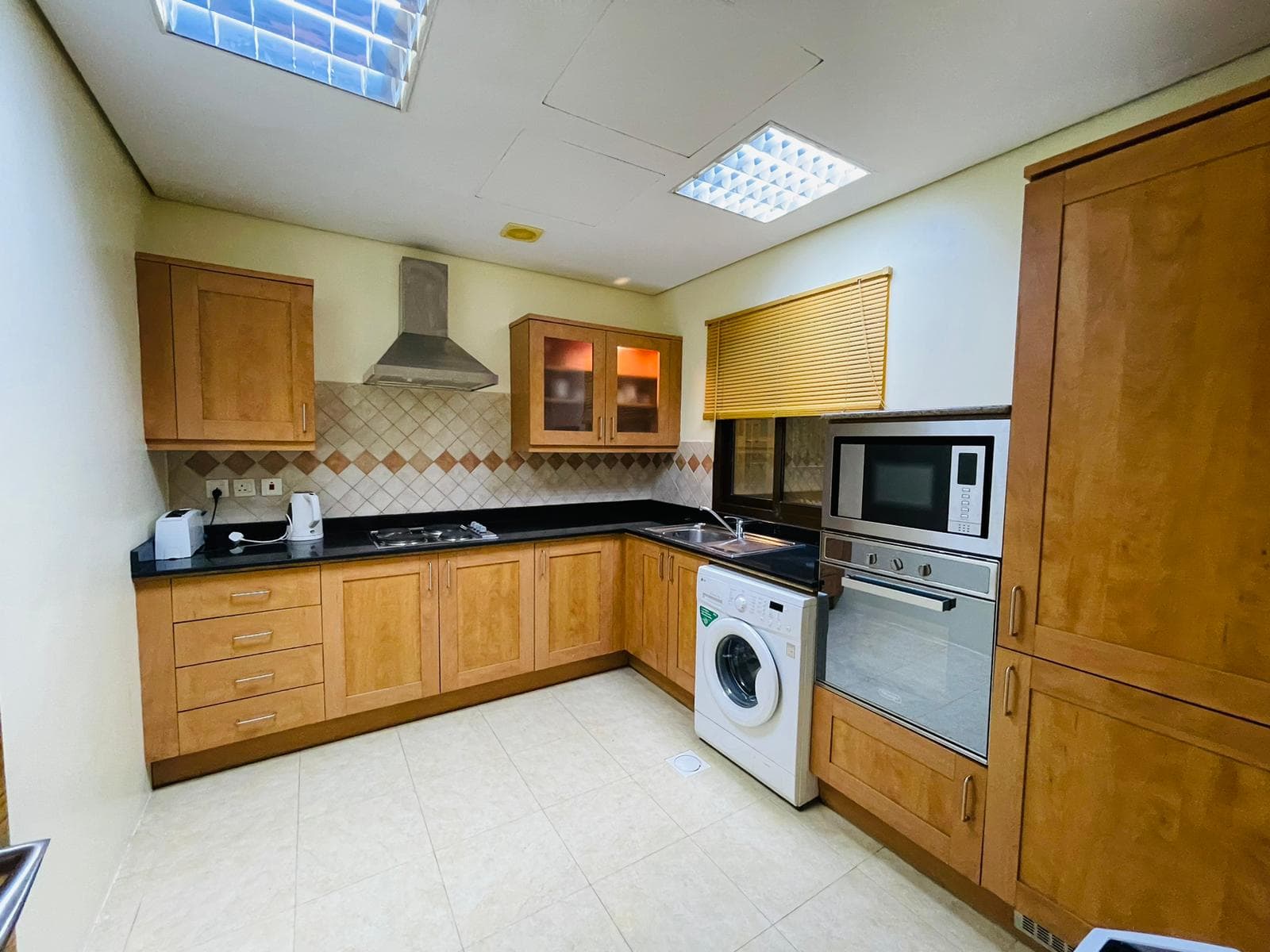 A modern kitchen with wooden cabinets, built-in appliances, and a washing machine under a countertop in a furnished apartment.