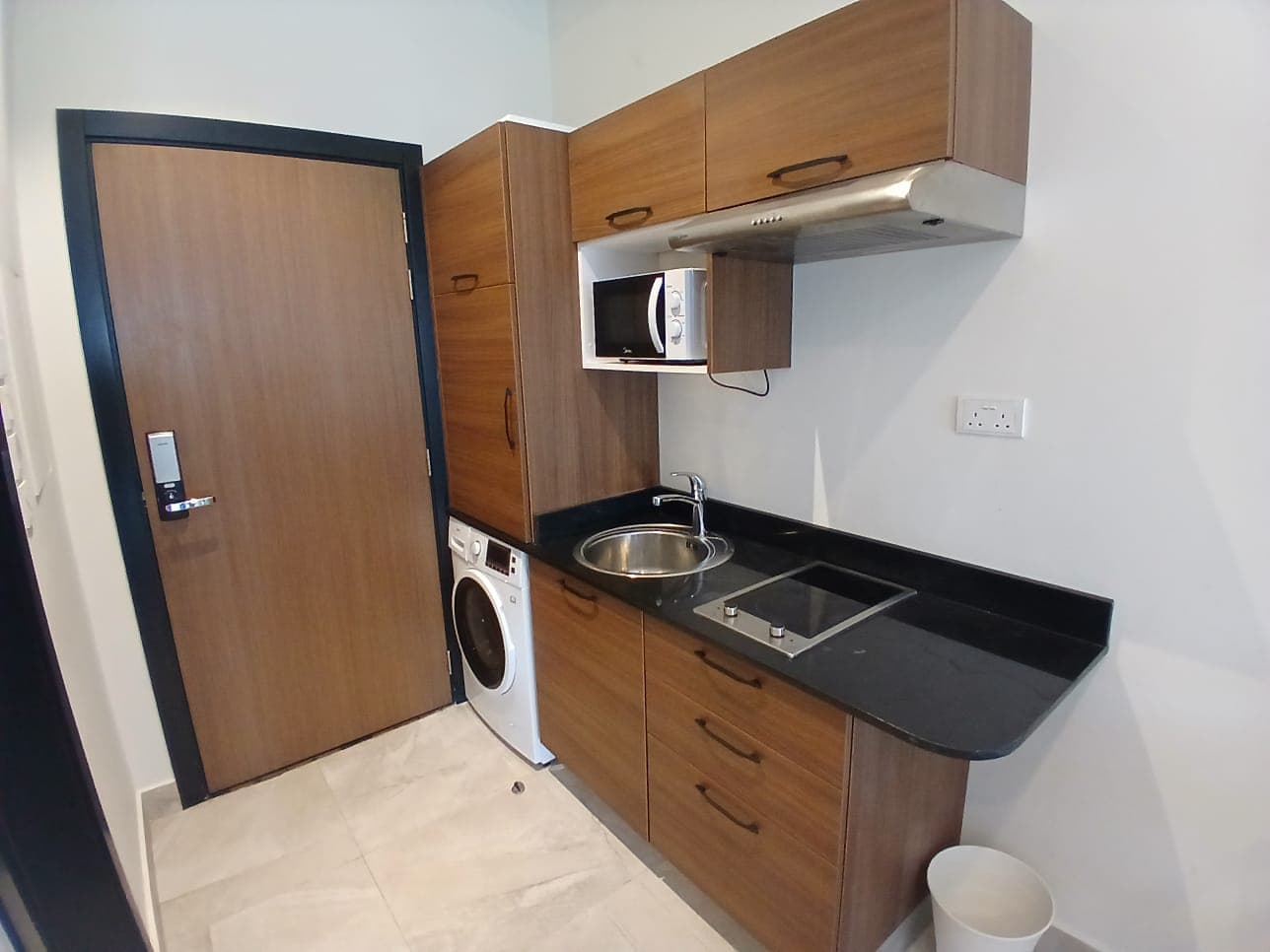 Modern small kitchen in a luxury studio for rent, with wooden cabinets, black countertop, built-in appliances, and an open door in Busiteen.