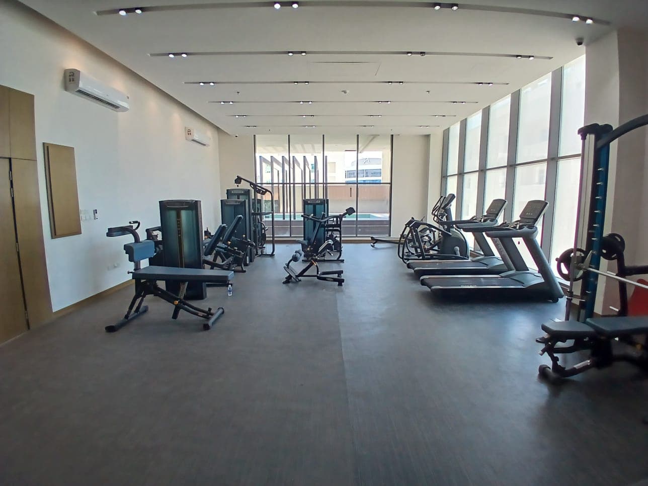 A spacious luxury studio gym in Busiteen with various exercise machines including treadmills, ellipticals, and weight stations, lit by natural light from large windows.