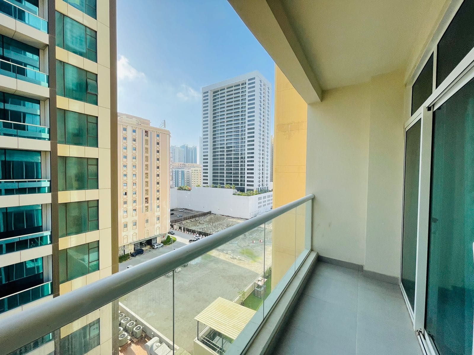 View from a luxury apartment balcony in Juffair showing neighboring buildings and a small park under a clear blue sky.