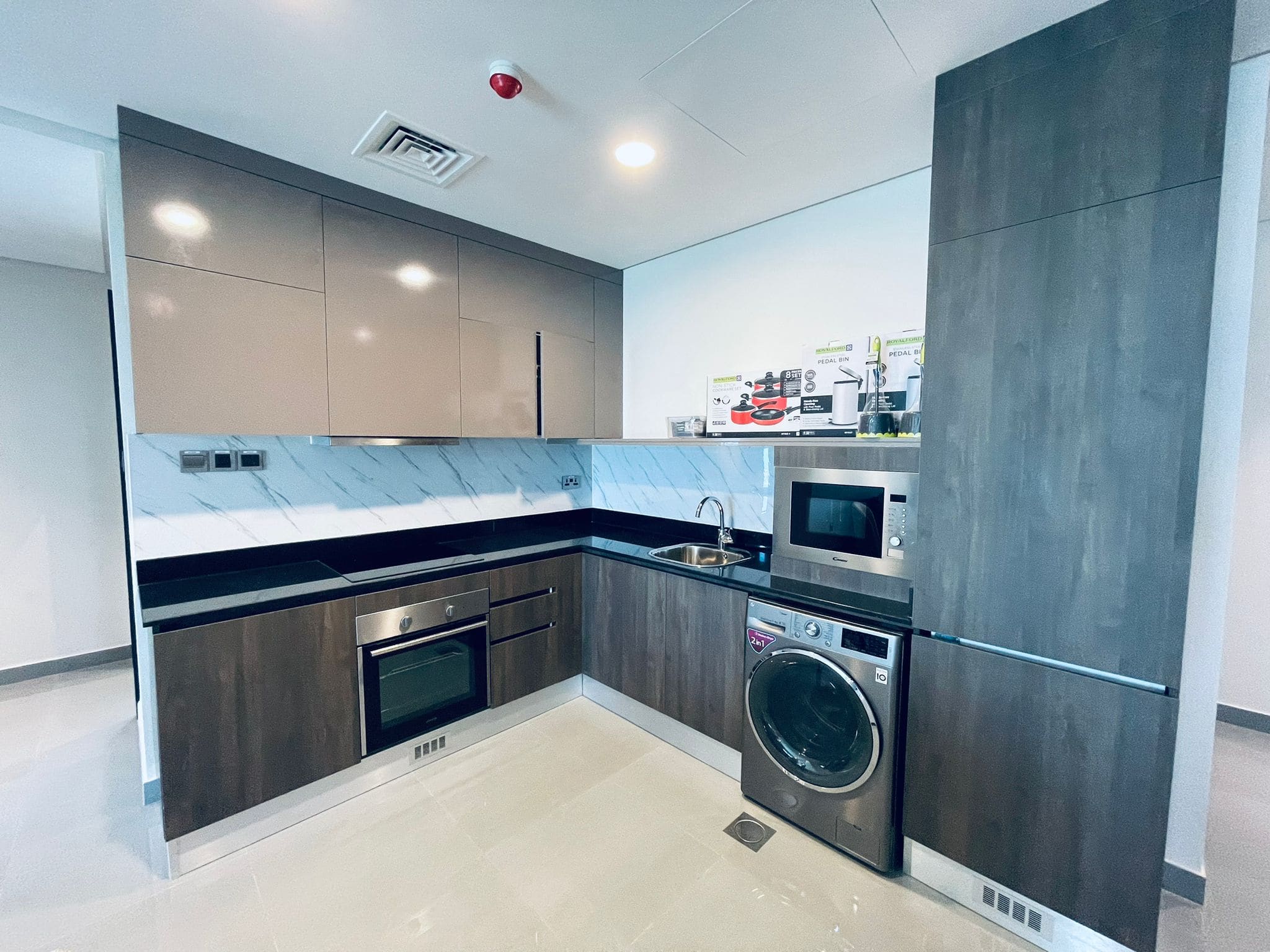 A modern kitchen with gray cabinetry, stainless steel appliances, a washing machine, and marble countertops.