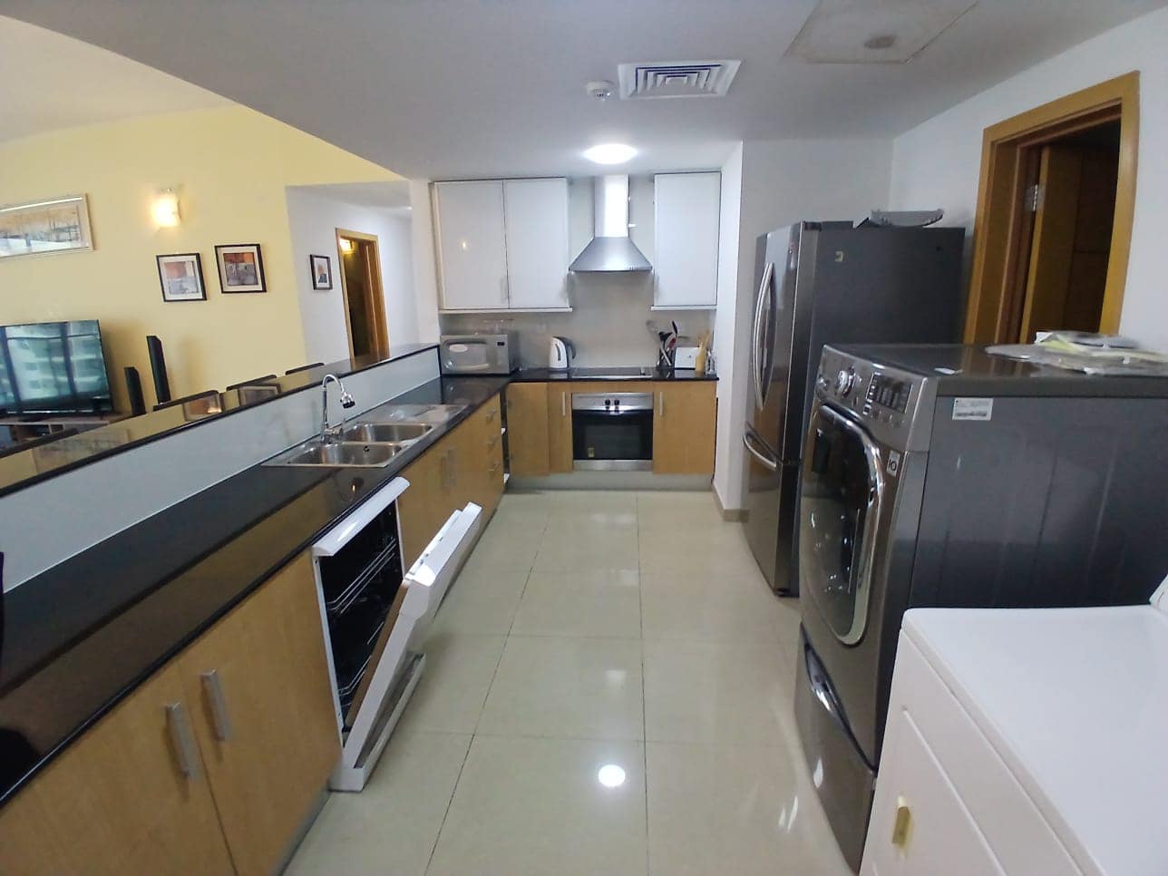 Modern kitchen interior in a flat in Amwaj with stainless steel appliances, wooden cabinets, and a narrow layout, featuring a double-door refrigerator and wall-mounted oven.