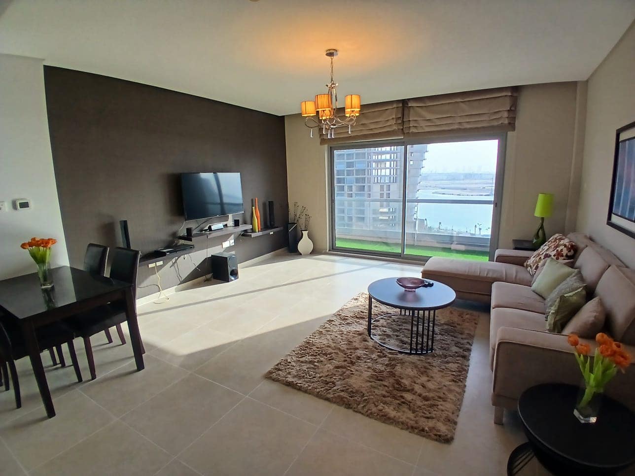 Modern living room in a rental property with a sectional sofa, TV, dining area, and large window overlooking water.