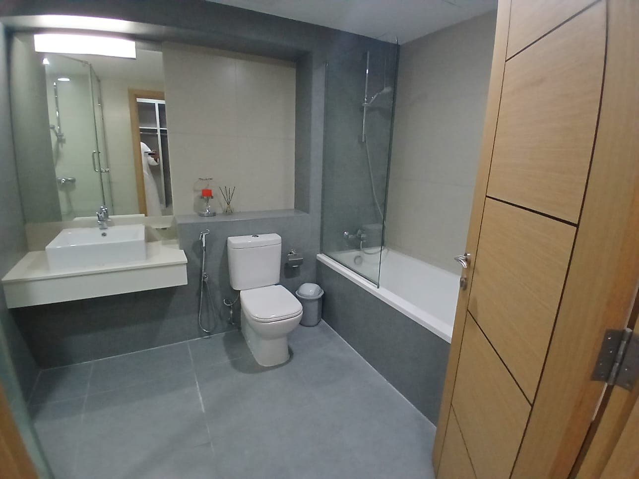 Modern bathroom interior in a flat for rent with a shower, bathtub, toilet, sink, and wooden cabinets. Neutral color scheme.