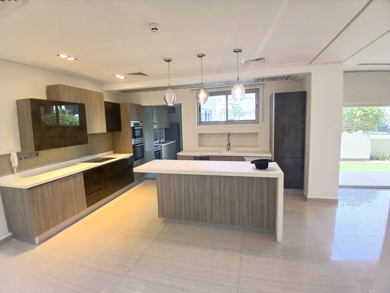 Modern villa with wooden cabinets, white countertops, an island, and pendant lights.