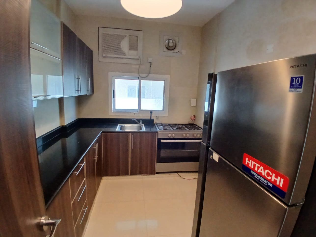 A compact, modern kitchen featuring stainless steel appliances, wooden cabinets, and tiled floor.