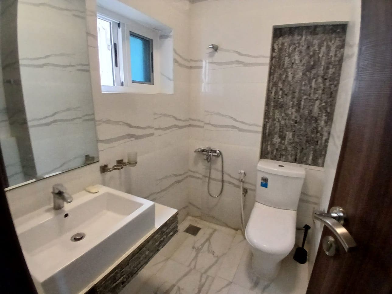 Modern bathroom interior with gray marble walls in an amazing apartment, featuring a white sink, toilet, and a shower with a glass door.