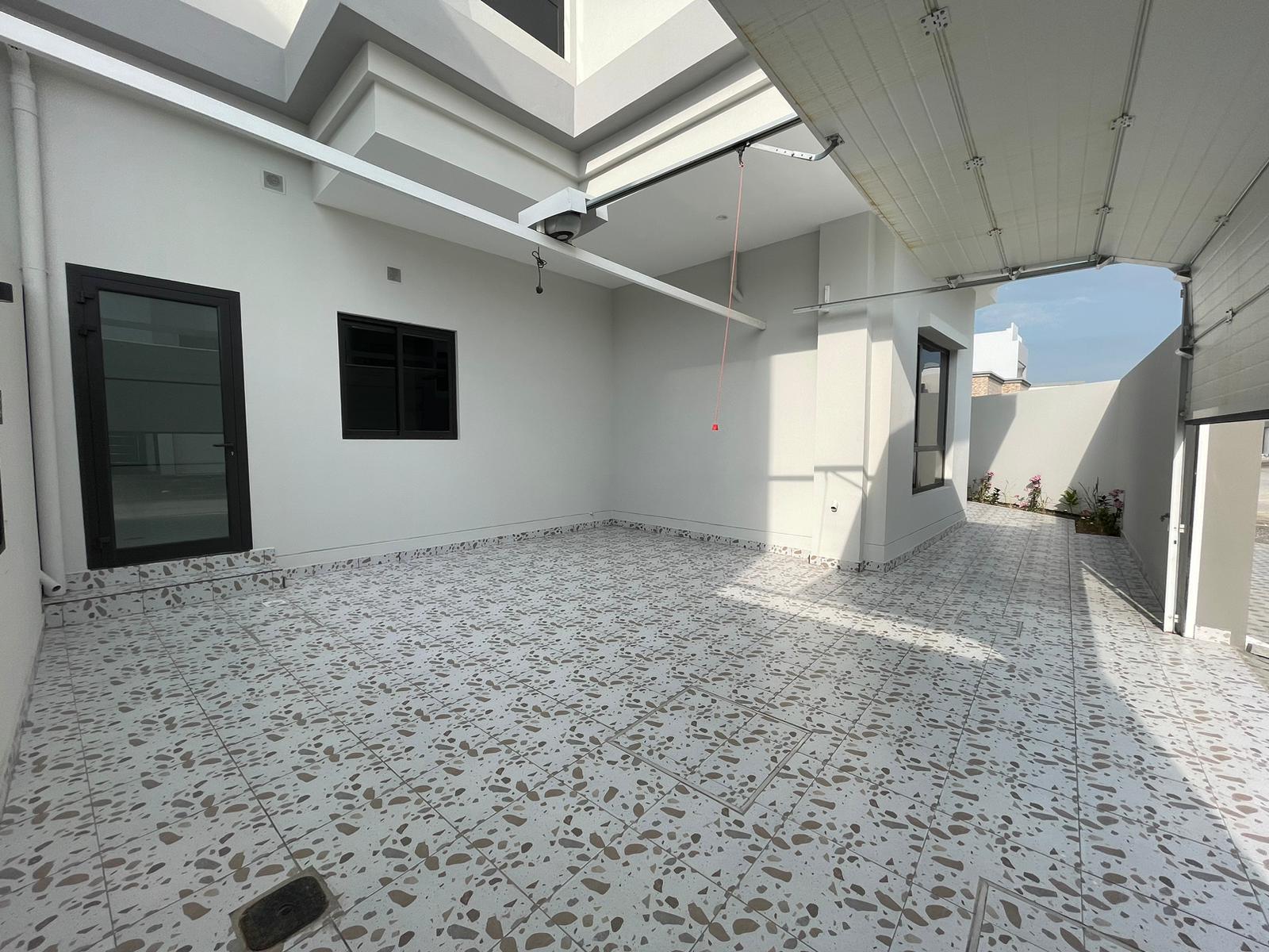 Spacious, empty outdoor patio with patterned flooring, white walls, and a partially open roof in a great location.