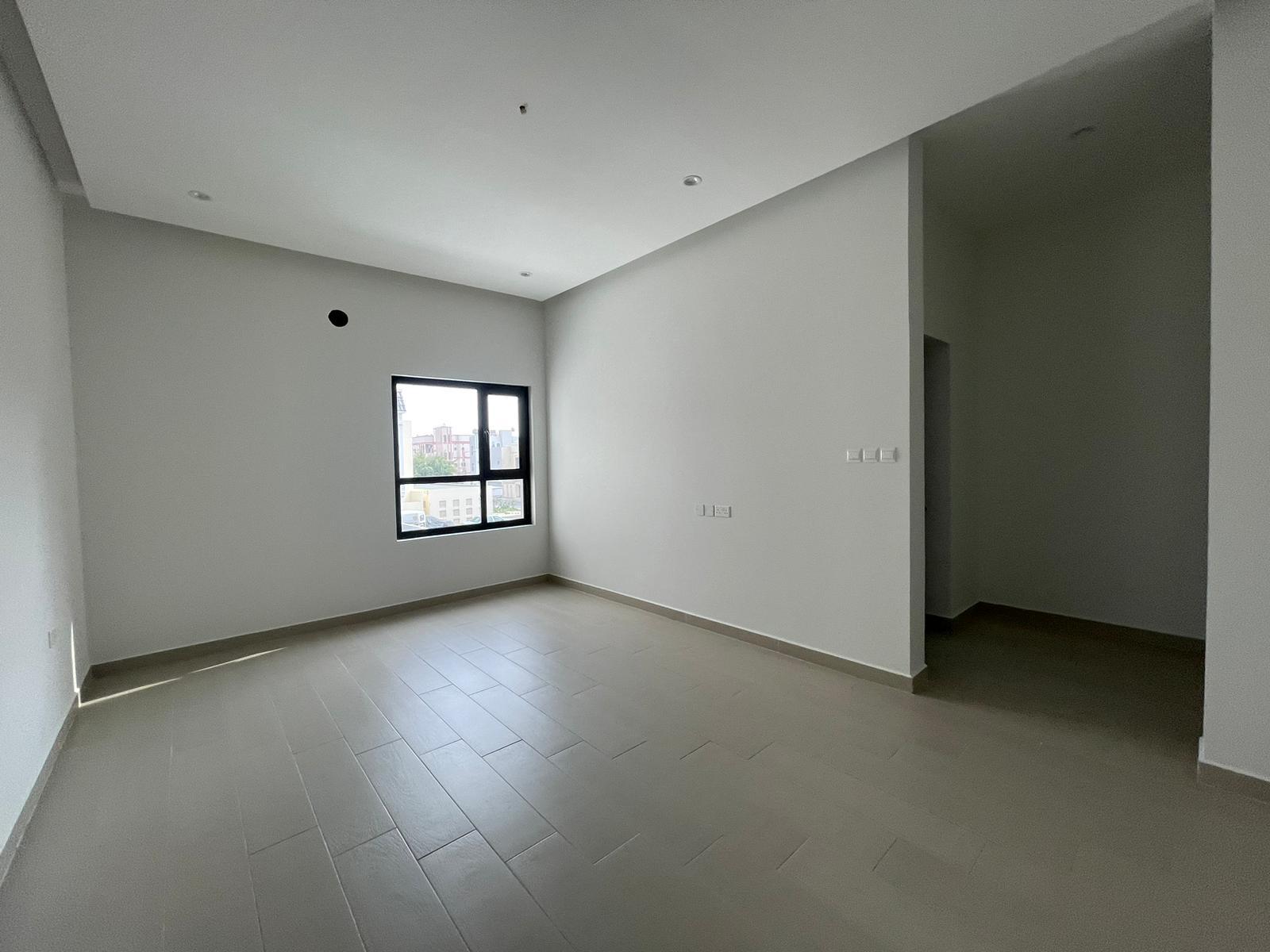 Empty modern villa room in Bani Jamra with white walls, a large window, and gray tile flooring.