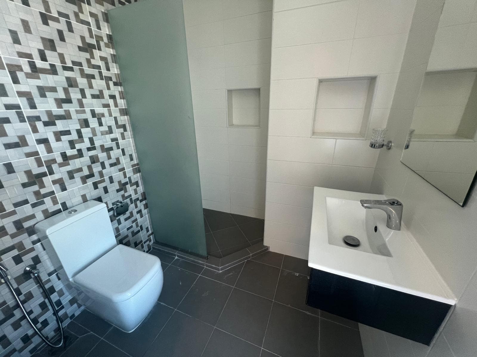 Luxury modern bathroom with mosaic tiled wall, white toilet, and wall-mounted sink.