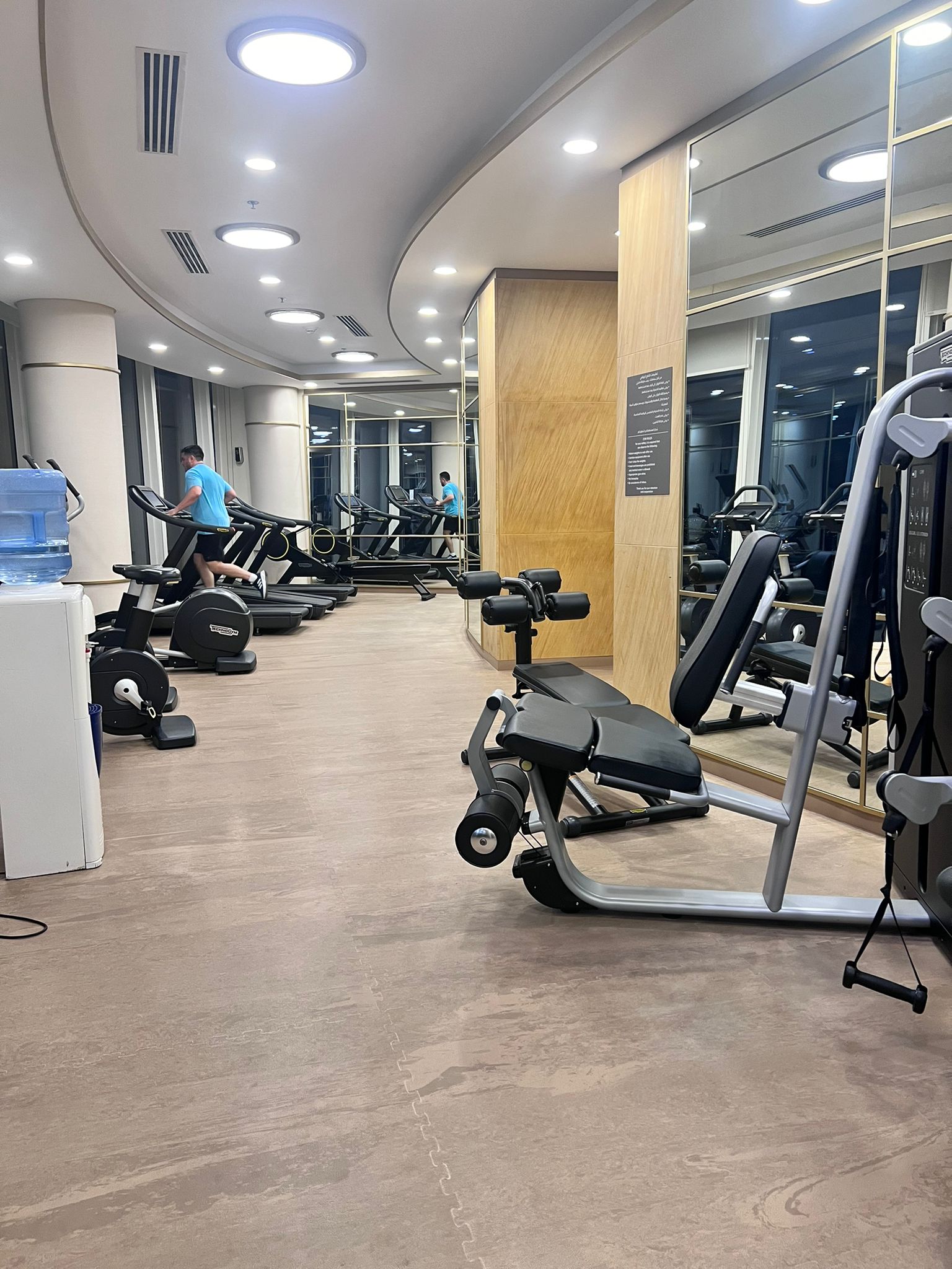 A person in a blue shirt is exercising on a treadmill in a well-lit gym filled with various cardio and strength training equipment, providing an ideal setting for an effective auto draft workout plan.