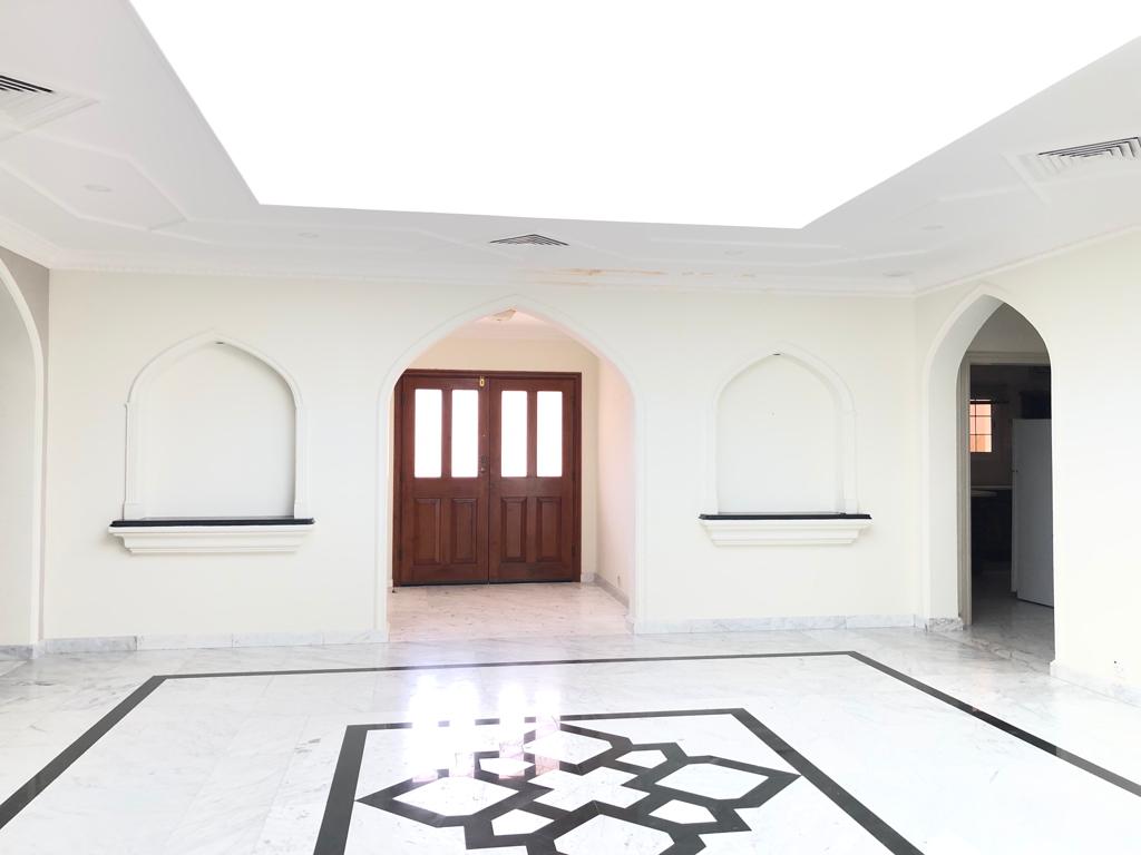 A semi-furnished, spacious room with marble flooring, an ornate black and white geometric pattern, arched wall niches, and double wooden doors under a brightly lit ceiling is one of the highlights of this stunning 3-bedroom villa.