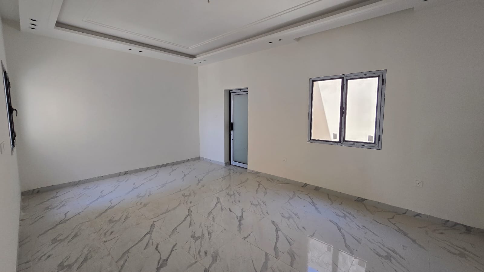 A vacant, well-lit room with white walls, a window, a door, and glossy white marble floor tiles in the desirable Damistan area. New villas for sale nearby offer modern amenities and stunning finishes.