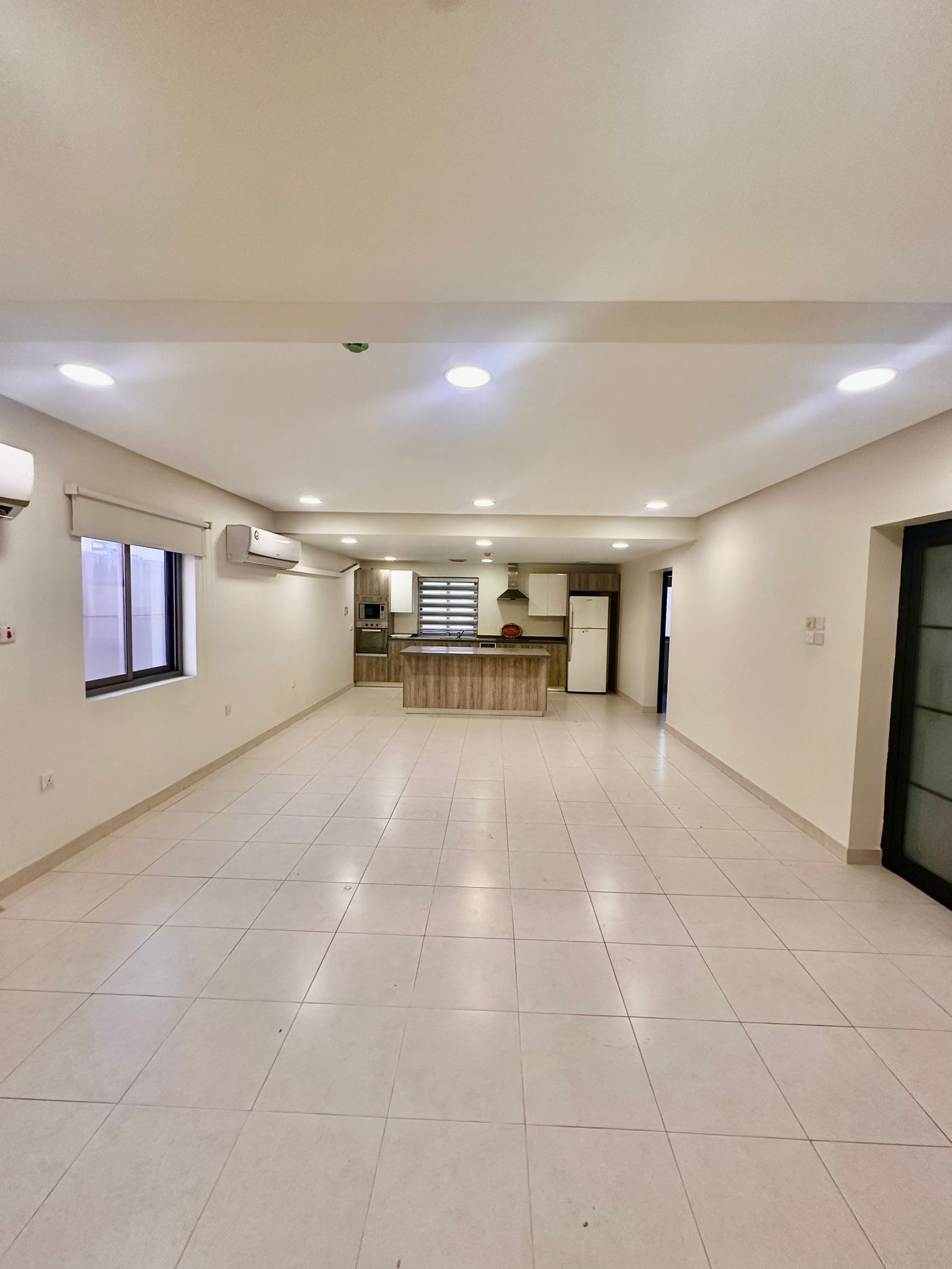 Spacious Triplex Apartment featuring an unfurnished open-plan kitchen and living area with tiled floors, recessed lighting, air conditioning units, and large windows. Perfect for those seeking a modern yet comfortable living space in Shakurah.