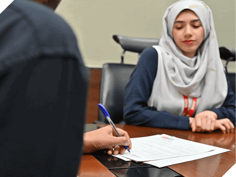 Two people at a meeting desk; as one signs a document with a pen, the other observes attentively, contemplating their House Me Career path.