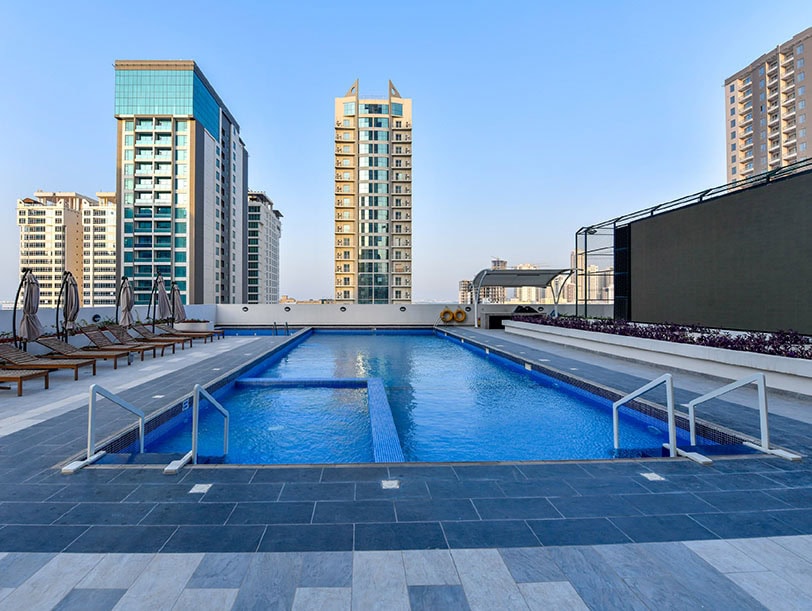 Experience the epitome of luxury with a rooftop pool featuring clear blue water, surrounded by lounge chairs and stunning high-rise views, all nestled in the vibrant landscape showcased by House Me Bahrain's premier commercial real estate services.