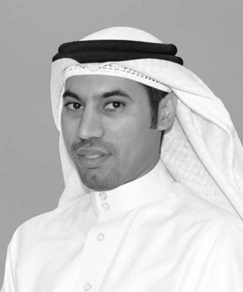 A man wearing a white thobe and a traditional headscarf looks directly at the camera against a plain gray background, embodying the professionalism and global reach of US commercial real estate services.