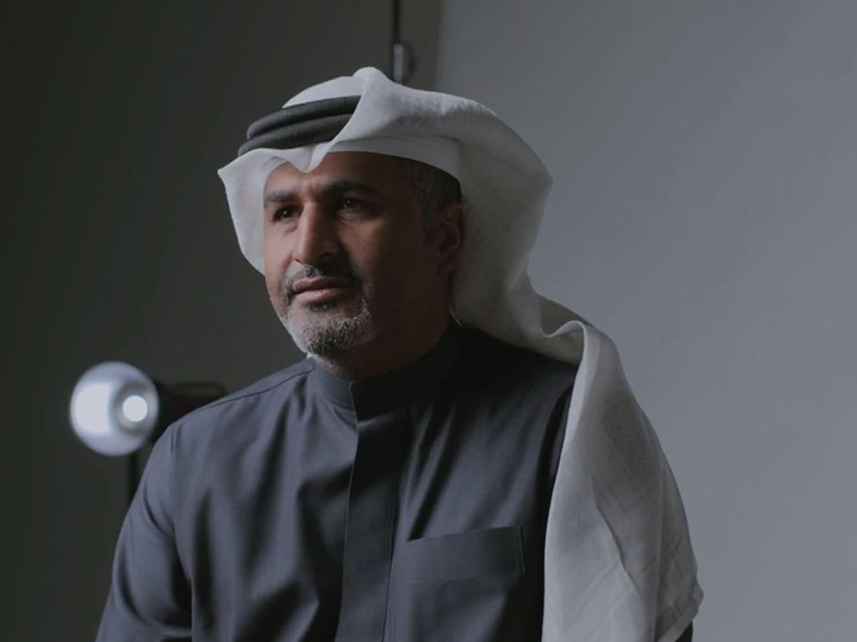 A man in traditional attire sits in front of a gray background, illuminated by a light source behind him, embodying a new vision for this era.