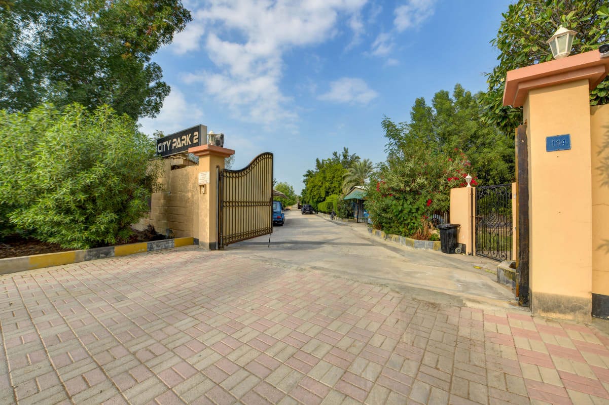 Entrance gate to a residential area labeled "City Park 2," with a partially open gate, paved driveway, trees, and buildings visible inside.