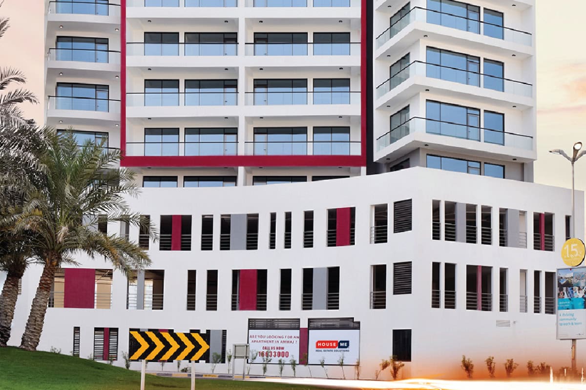 A modern multi-story building with white and red accents, glass balconies, and palm trees in front; a black and yellow road sign and a speed limit sign are visible.