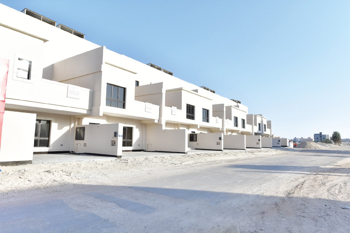 A row of modern, white, two-story townhouses with garages in a new housing development under clear blue sky.